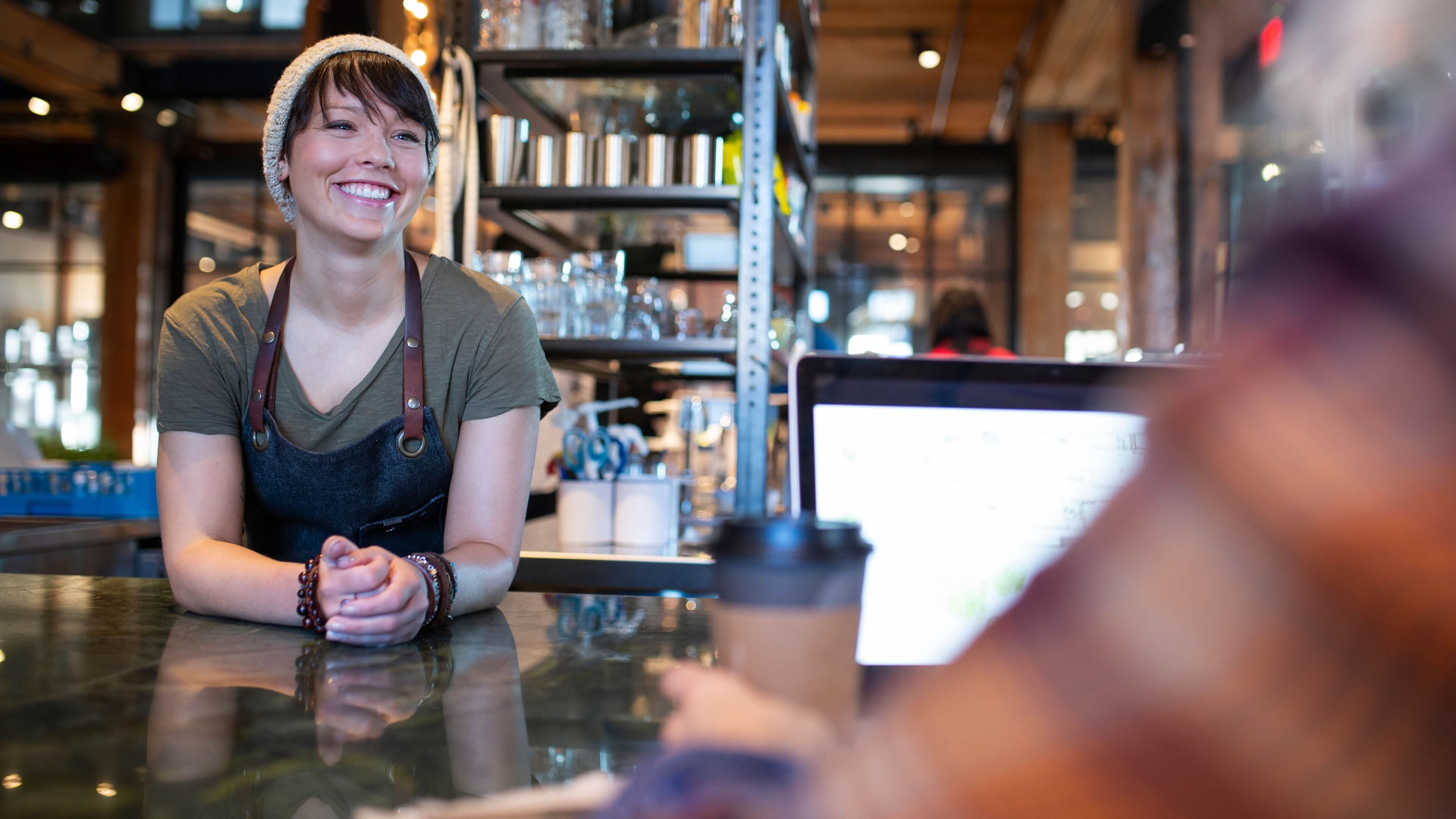 Barista talking to woman at laptop in coffee shop