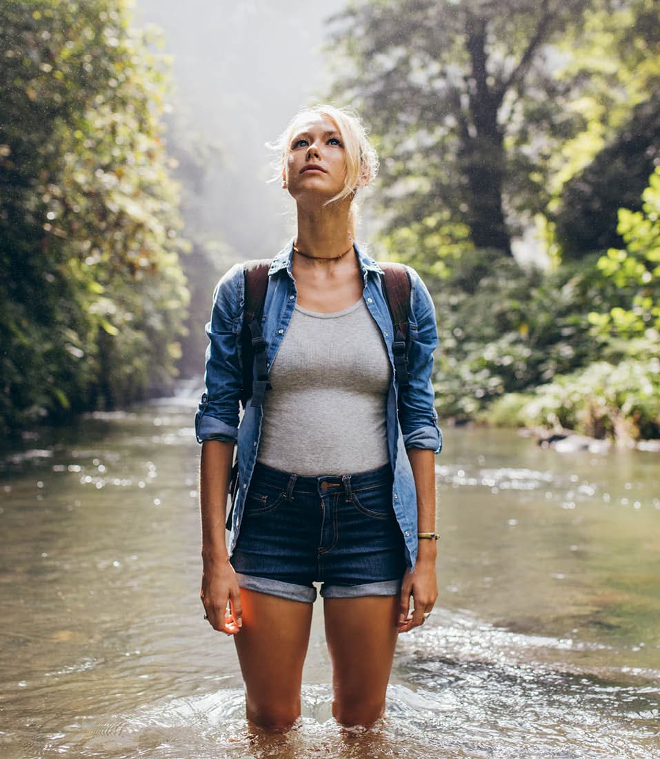 Attractive young female hiker with backpack standing in a wilderness stream. Caucasian young woman in creek looking away.; Shutterstock ID 464521697; purchase_order: -; job: -; client: -; other: -